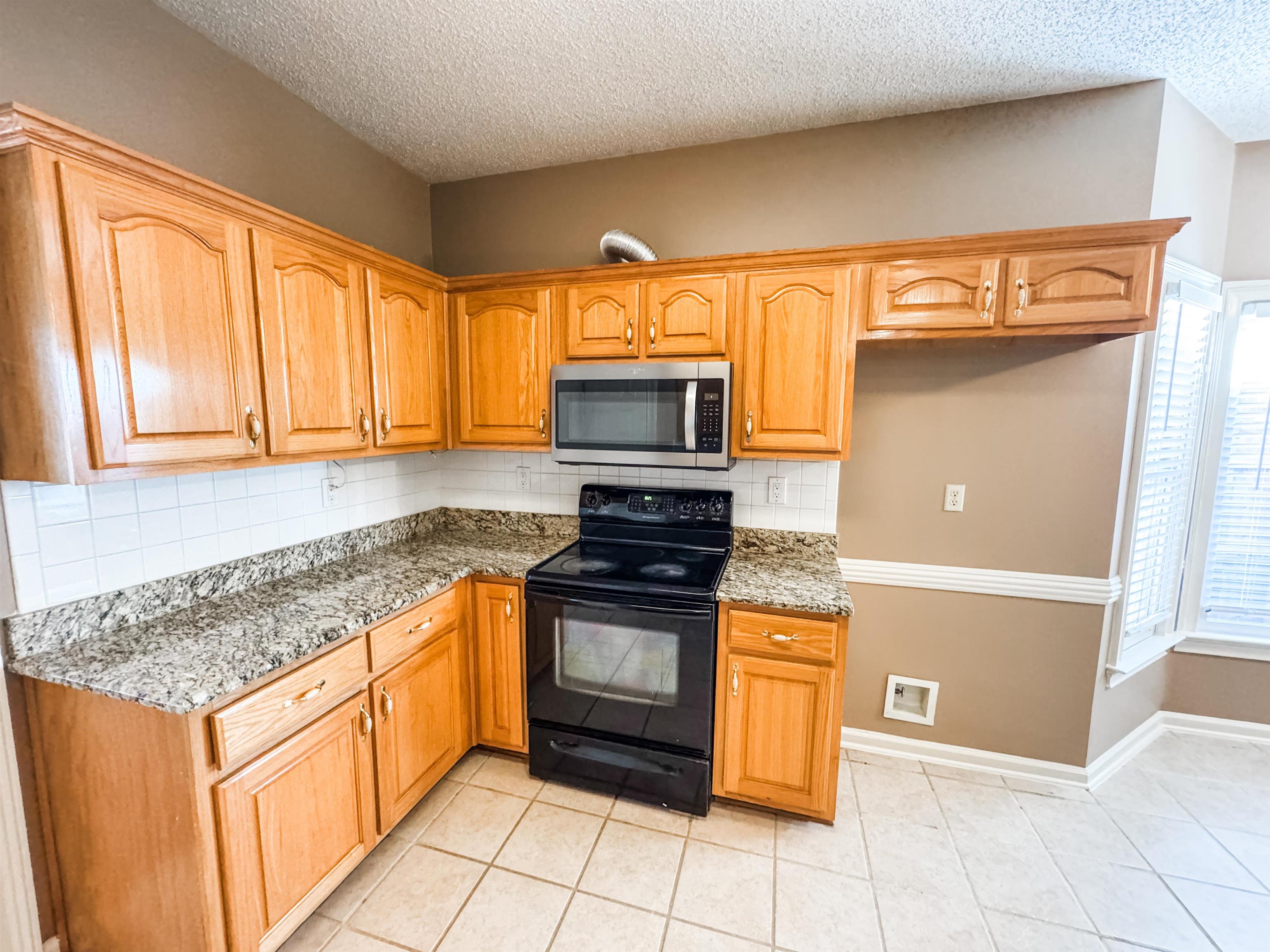 158 Eulas Ridge Cove Collierville, TN 38017 - Photo 7 of 18 Kitchen with light stone counters, stainless steel microwave, tasteful backsplash, black / electric stove, and light tile patterned flooring