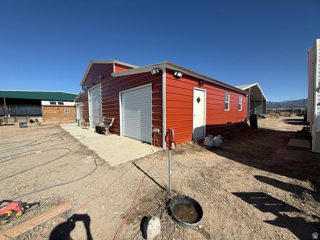 3550 North River Ln Road East Panguitch, UT 84759 - Photo 2 of 25 Red metal-sided structure featuring multiple roll-up garage doors, a pedestrian entrance, and exposed exterior lighting