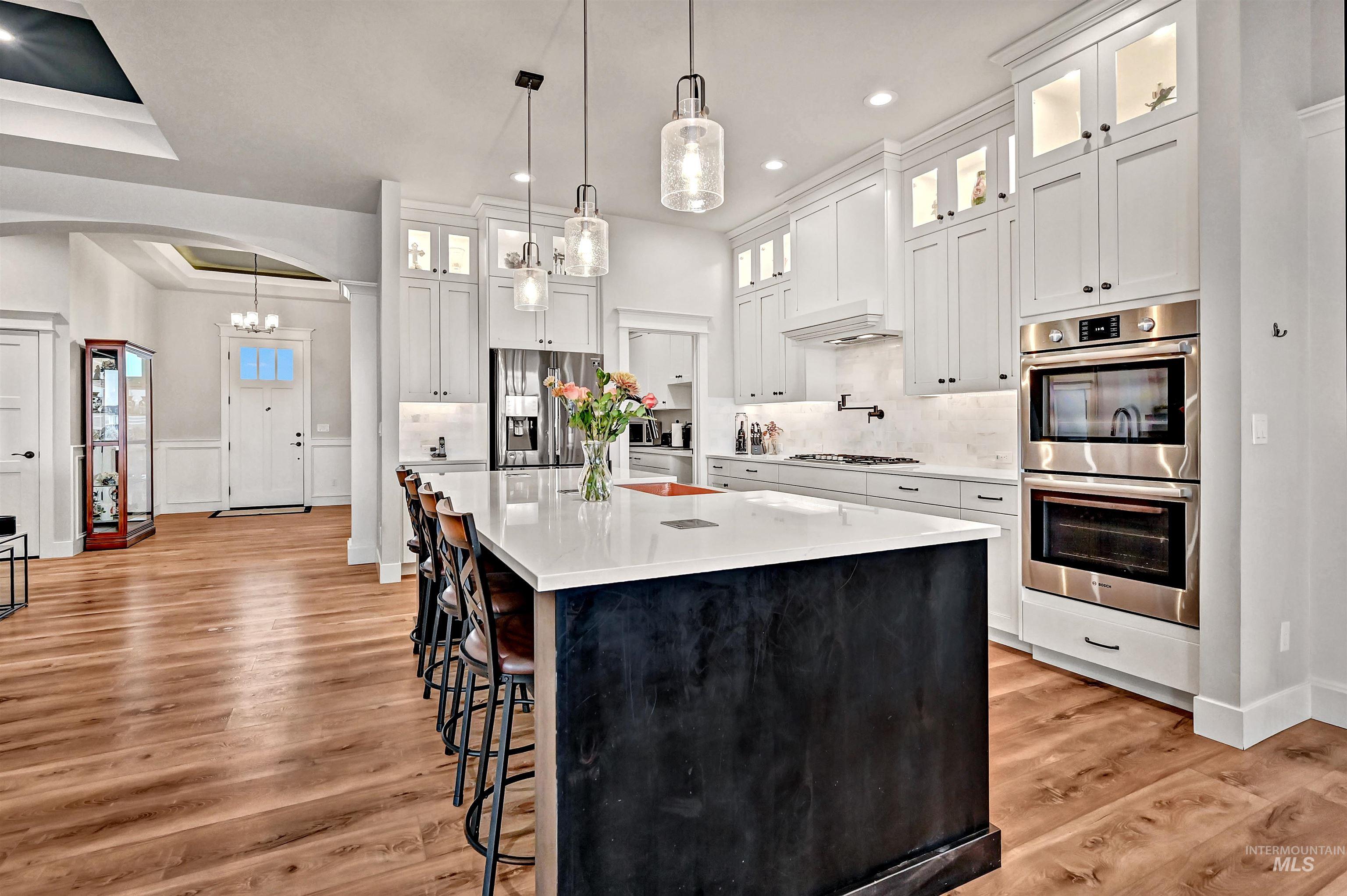 14964 Mortensen Court Caldwell, ID 83607 - Photo 12 of 38 Kitchen featuring glass insert cabinets, a breakfast bar, white cabinetry, appliances with stainless steel finishes, and arched walkways