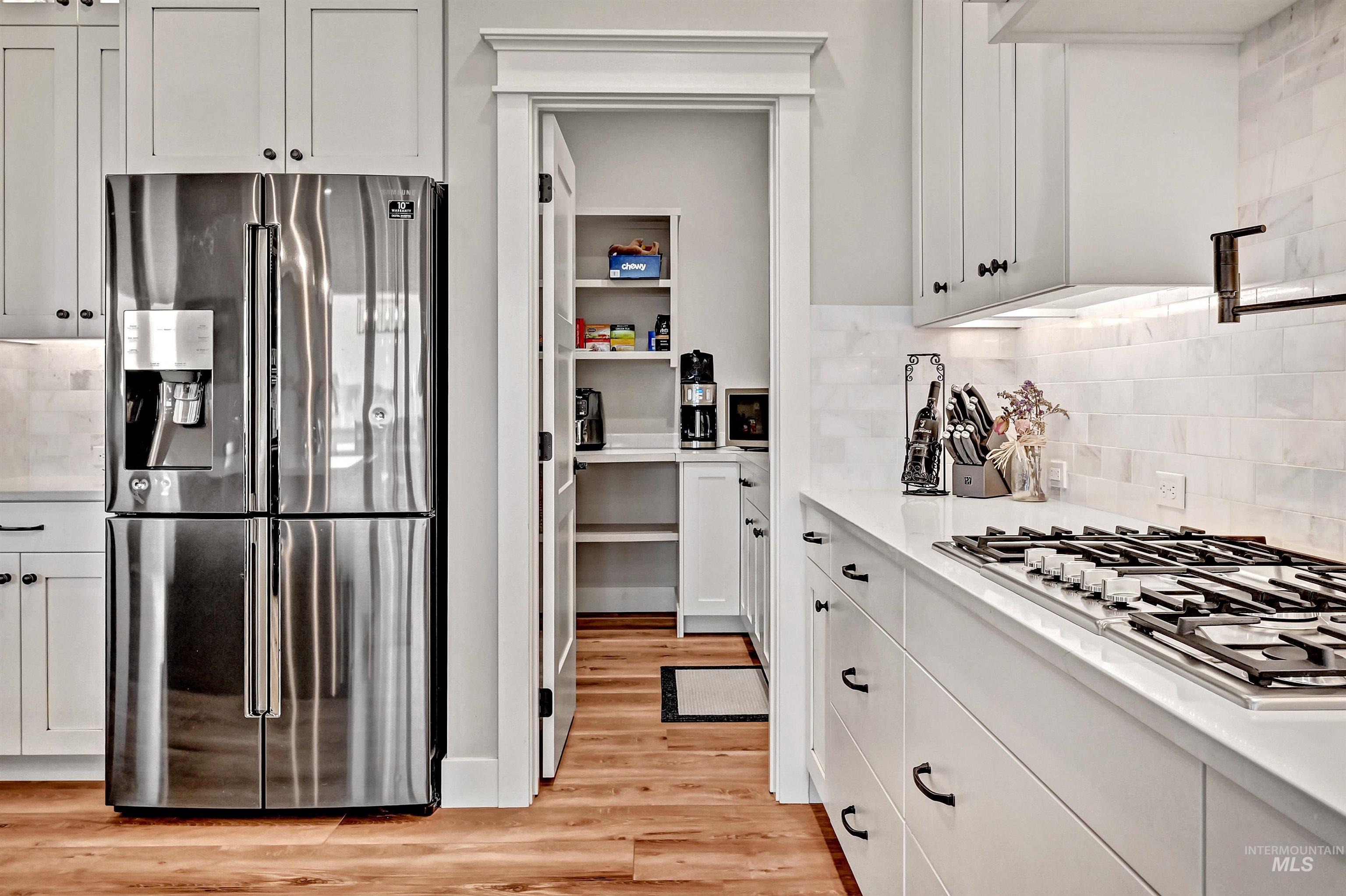 14964 Mortensen Court Caldwell, ID 83607 - Photo 13 of 38 Kitchen featuring stainless steel appliances, white cabinetry, light wood finished floors, backsplash, and light stone countertops