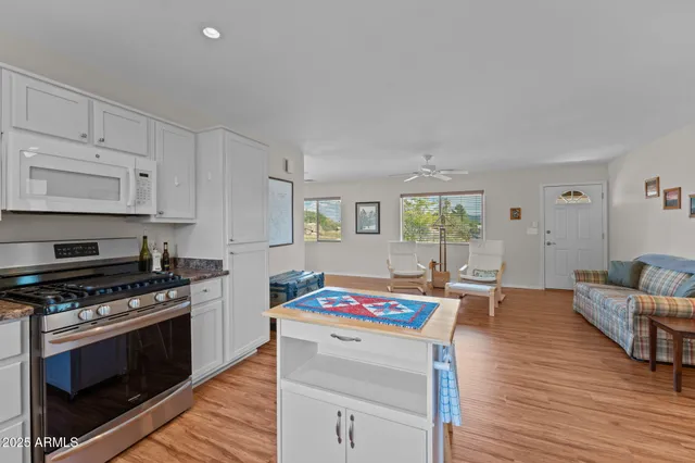 a open kitchen with stainless steel appliances a stove a sink dishwasher and white cabinets with wooden floor