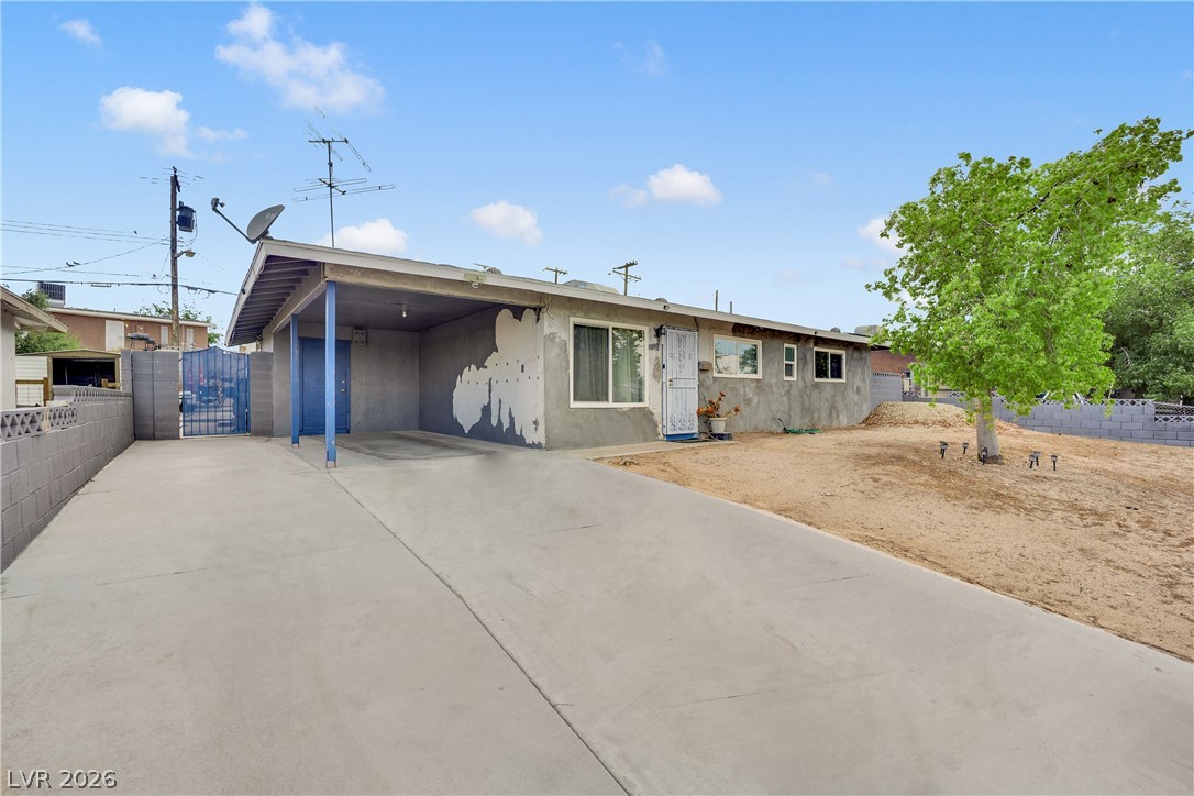 2221 Englestad Street North Las Vegas, NV 89030 - Photo 4 of 32 A long concrete driveway leads to a modest stucco residence with a covered carport and a sparse, arid front yard.
