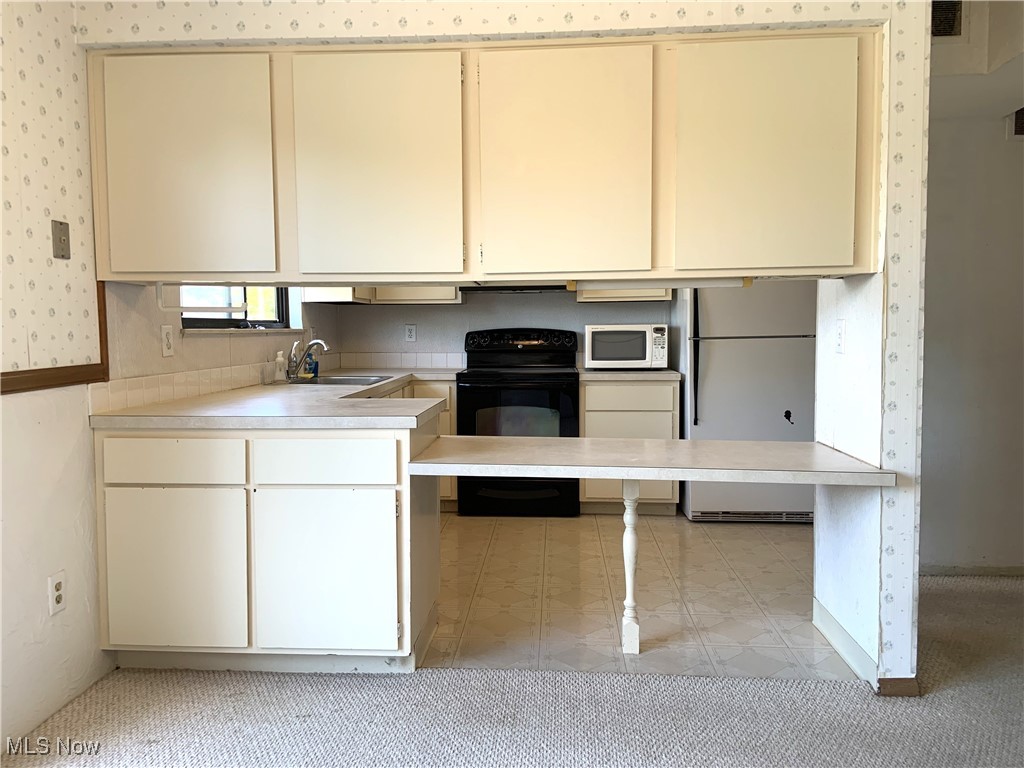 9956 Johnnycake Ridge Road, Unit D9 Painesville, OH 44077 - Photo 13 of 37 Kitchen featuring white appliances, cream cabinets, light countertops, and wallpapered walls