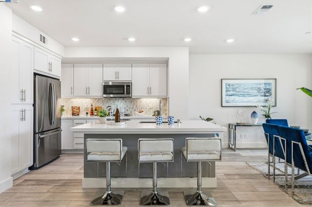 a kitchen with stainless steel appliances granite countertop a dining table chairs refrigerator and sink