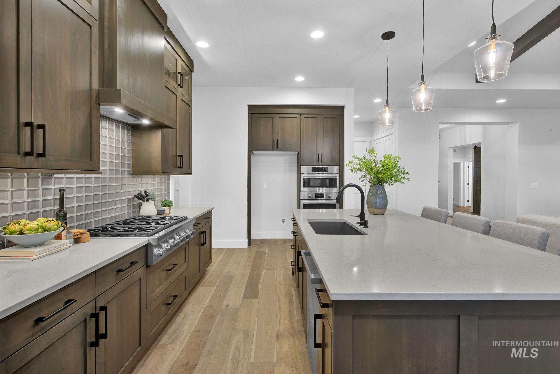 1911 West Timberstone Drive Eagle, ID 83616 - Photo 5 of 15 Kitchen with light stone countertops, light wood-style flooring, recessed lighting, dark brown cabinets, and pendant lighting