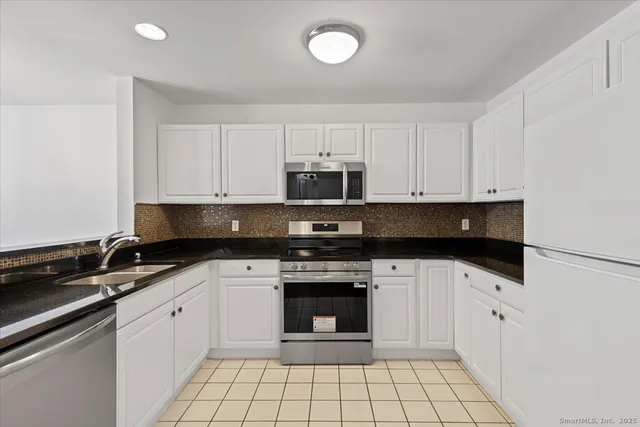 a white kitchen with granite countertop a stove top oven microwave and cabinets