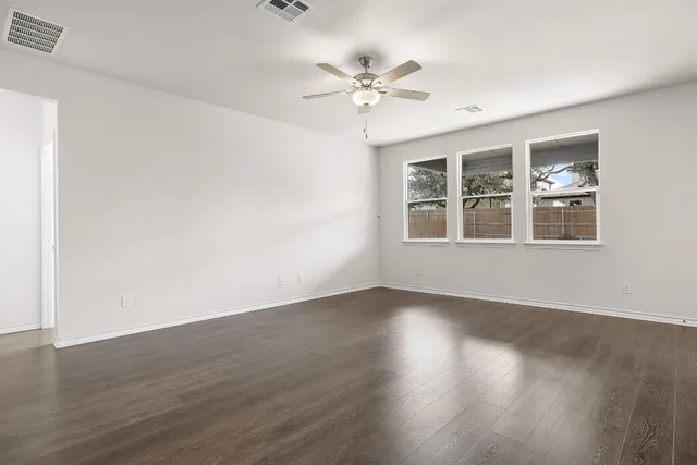 a view of an empty room with wooden floor and a ceiling fan