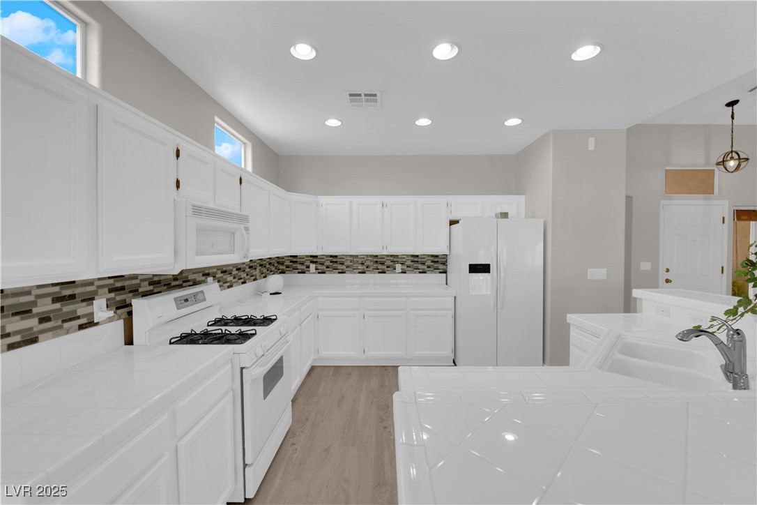 650 West Victory Road Henderson, NV 89015 - Photo 8 of 35 Kitchen featuring tile countertops, white appliances, white cabinetry, recessed lighting, and tasteful backsplash
