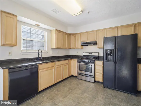 a kitchen with granite countertop stainless steel appliances a sink a refrigerator a window and cabinets