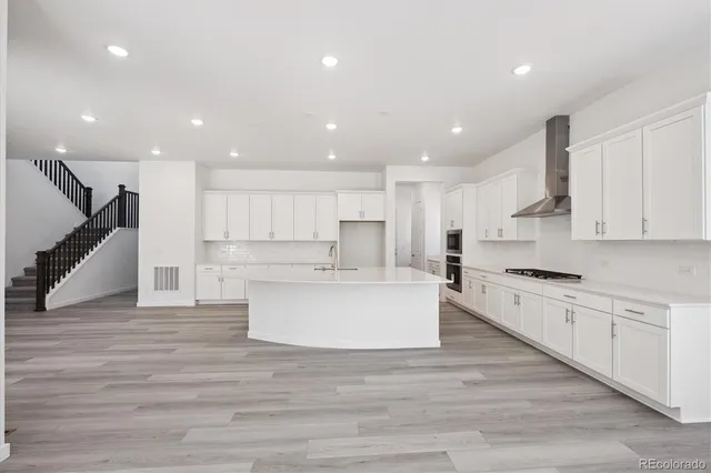 a large white kitchen with kitchen island sink refrigerator and white cabinets