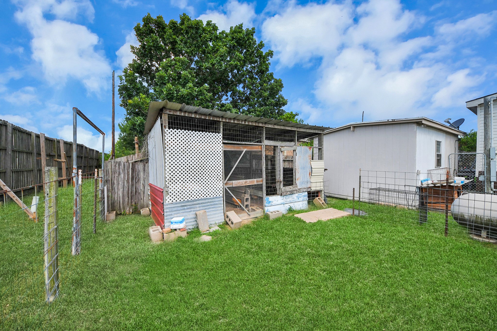 131 Kiowa Court Rosharon, TX 77583 - Photo 39 of 42 This photo features a fenced backyard with a small shed or animal enclosure on a grassy lawn. The area is bordered by a wooden fence and is adjacent to a neighboring structure, offering potential for outdoor use or storage.