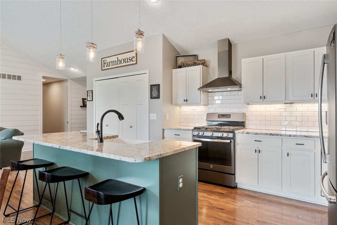 6517 Stone Road Medina, OH 44256 - Photo 12 of 47 Kitchen featuring wall chimney range hood, stainless steel appliances, sink, light hardwood / wood-style floors, and lofted ceiling