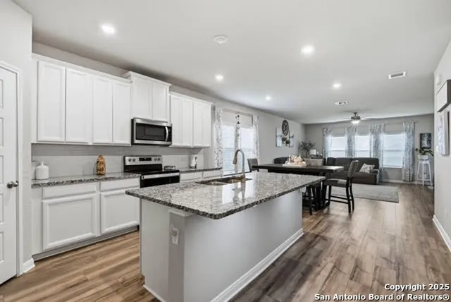 a kitchen with stainless steel appliances granite countertop wooden cabinets a sink a stove a dining table and chairs