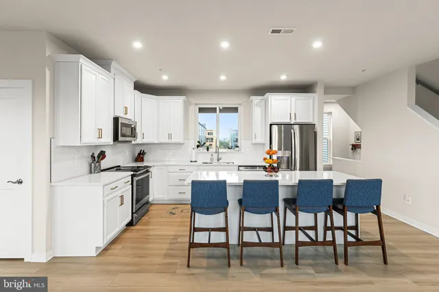 a kitchen with stainless steel appliances granite countertop a stove a sink a refrigerator a kitchen island with chairs and white cabinets