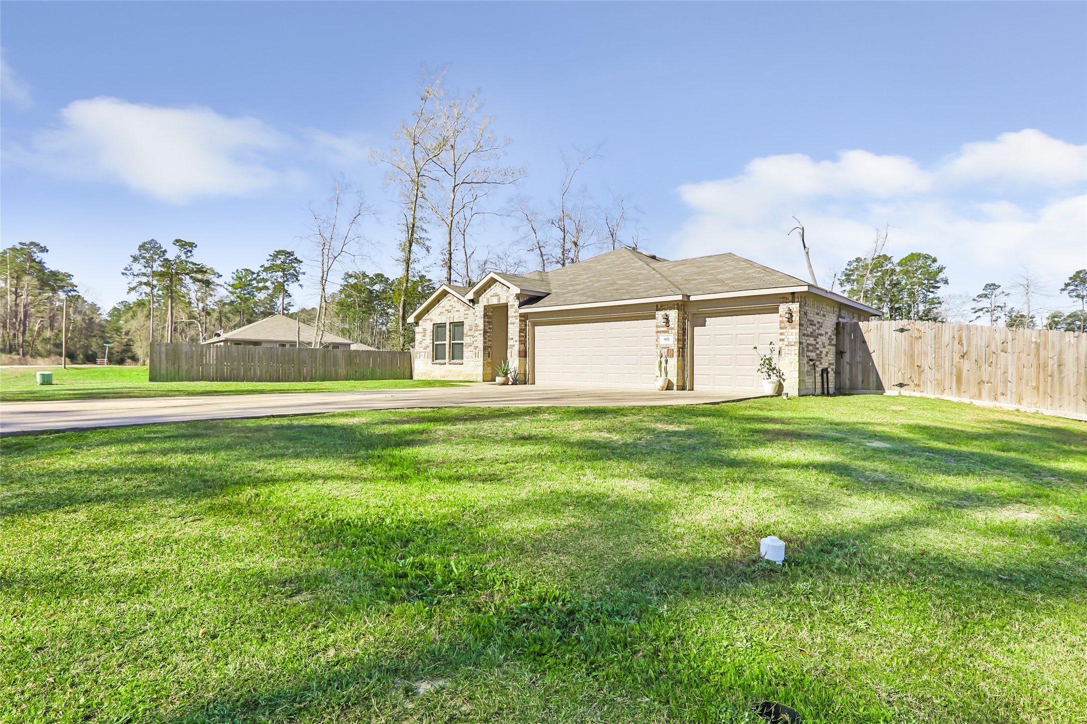 811 Republic Road New Caney, TX 77357 - Photo 3 of 37 This photo showcases a charming single-story home with a brick exterior and a three-car garage. It's set on a spacious, well-maintained lawn, surrounded by a wooden fence, and bordered by trees, offering privacy and a serene atmosphere.
