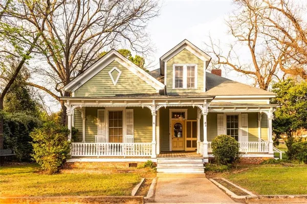 a view of a white house with a large windows and a yard with plants and large trees