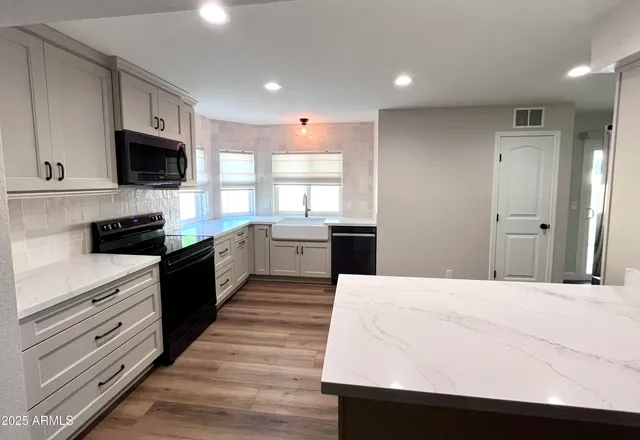 a kitchen with stainless steel appliances kitchen island granite countertop a stove top oven a sink dishwasher and a refrigerator with wooden floor