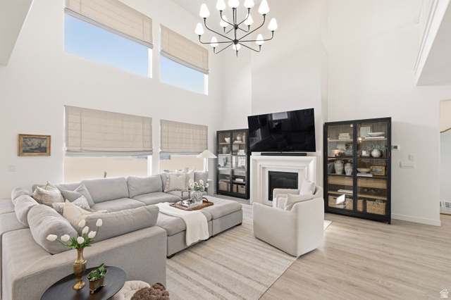 870 North Ada Loop Lehi, UT 84048 - Photo 7 of 51 Two-story living area featuring high ceilings, multiple window sets with integrated shades, a central fireplace with an ornate mantel, wood-finish flooring, and a modern chandelier