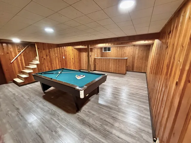 a room with wooden floor pool table and chairs