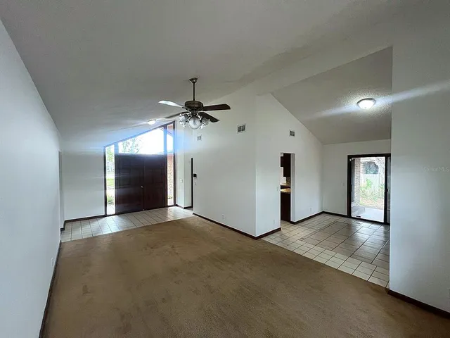 an empty room with chandelier fan and windows