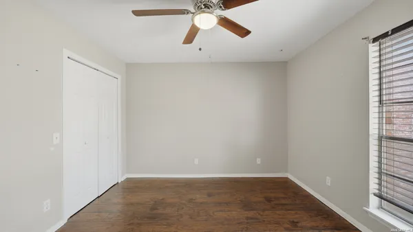 an empty room with wooden floor fan and windows