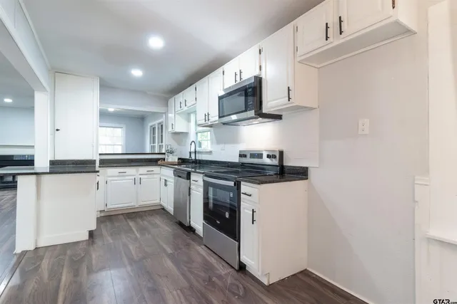 a kitchen with stainless steel appliances white cabinets a sink a stove a microwave and wooden floors