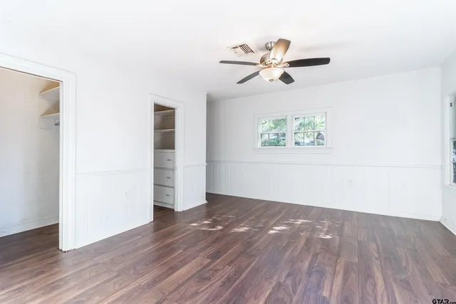 an empty room with wooden floor chandelier fan and windows