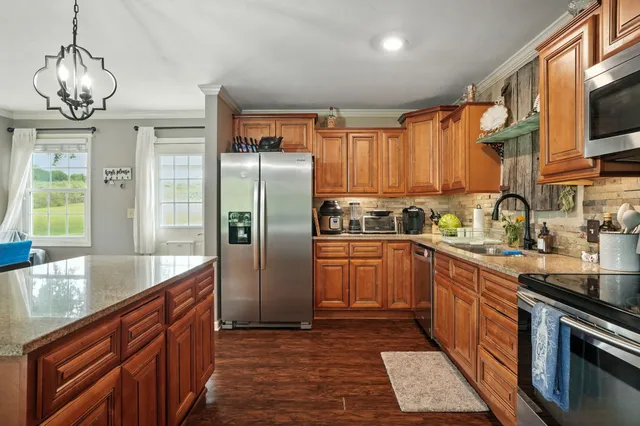 a kitchen with stainless steel appliances granite countertop a refrigerator a sink dishwasher a stove with wooden cabinets and floor