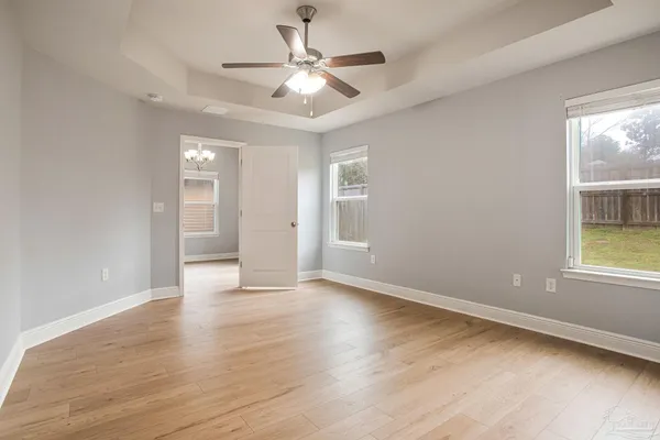 an empty room with wooden floor chandelier fan and windows