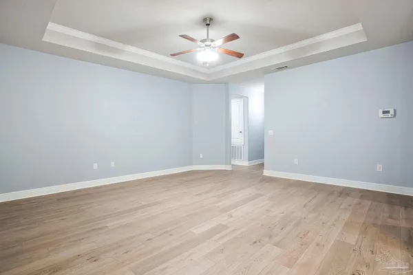 a view of an empty room with chandelier fan and wooden floor