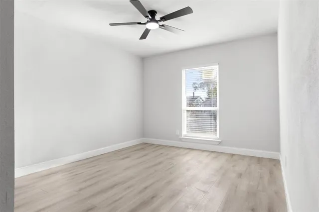 an empty room with wooden floor ceiling fan and windows