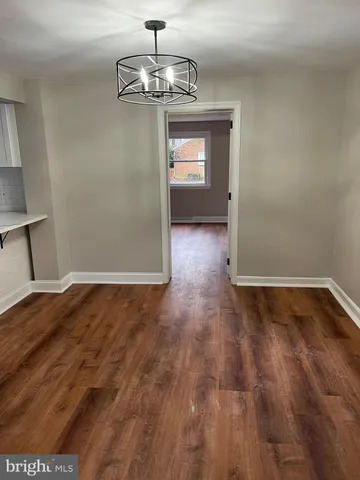 a view of empty room with wooden floor and kitchen