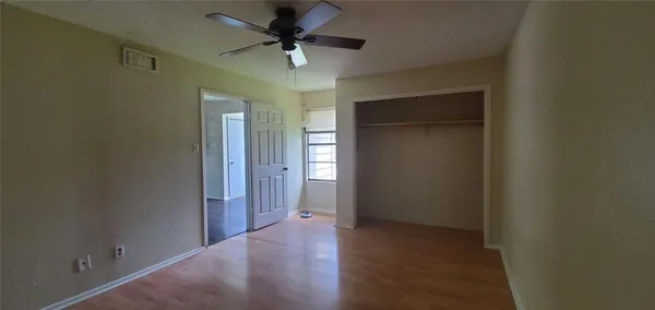 an empty room with wooden floor closet and fan