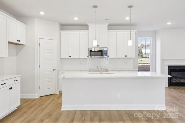 a large kitchen with stainless steel appliances granite countertop a stove a sink a refrigerator and white cabinets with wooden floor