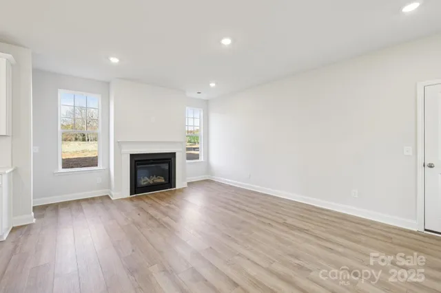 a view of an empty room with wooden floor fireplace and a window
