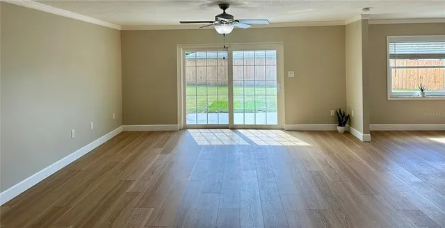 an empty room with wooden floor chandelier fan and windows