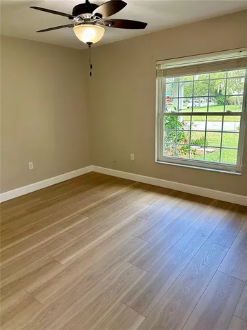 an empty room with wooden floor fan and windows