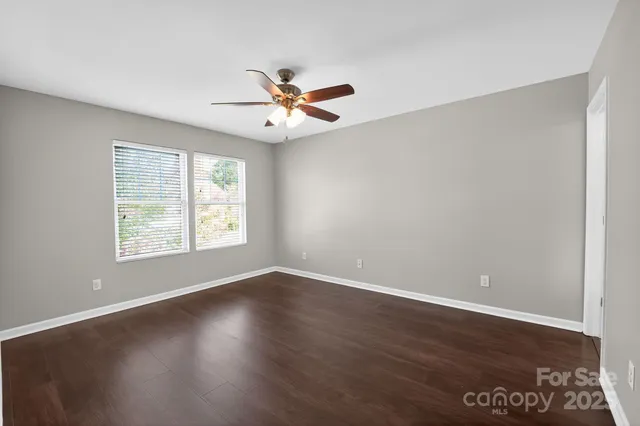 an empty room with wooden floor fan and windows