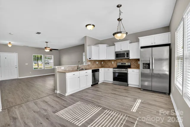 a kitchen with granite countertop a refrigerator a stove and white cabinets with wooden floor