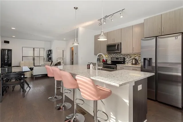 a kitchen with stainless steel appliances kitchen island granite countertop a refrigerator a stove a sink a dining table and chairs with wooden floor