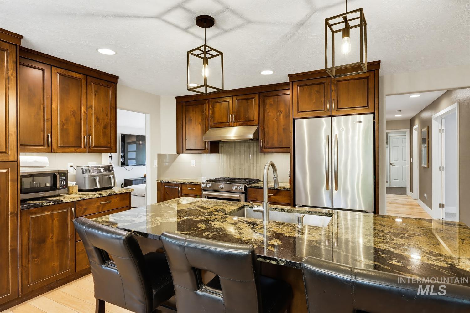 369 South Winthrop Way Boise, ID 83709 - Photo 15 of 50 Kitchen featuring an island with a built-in sink and seating, dark wood-finish cabinetry, stainless steel appliances, and pendant lighting