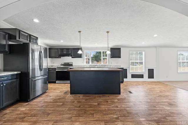 a large kitchen with stainless steel appliances kitchen island granite countertop a refrigerator a sink dishwasher a oven and a dining table with wooden floor