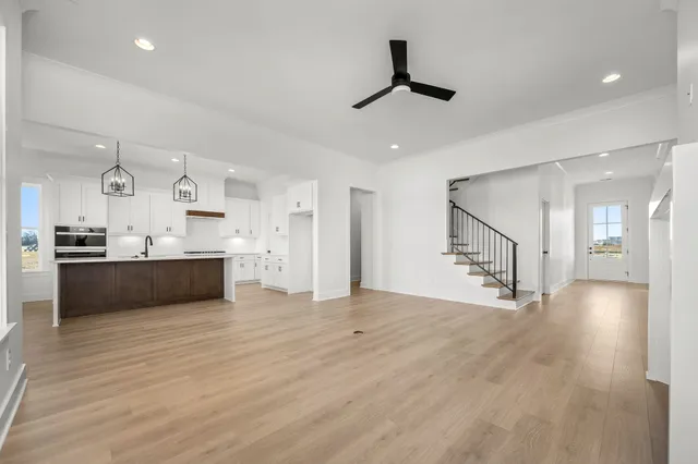 a large kitchen with stainless steel appliances kitchen island granite countertop a stove a sink a refrigerator and white cabinets with wooden floor