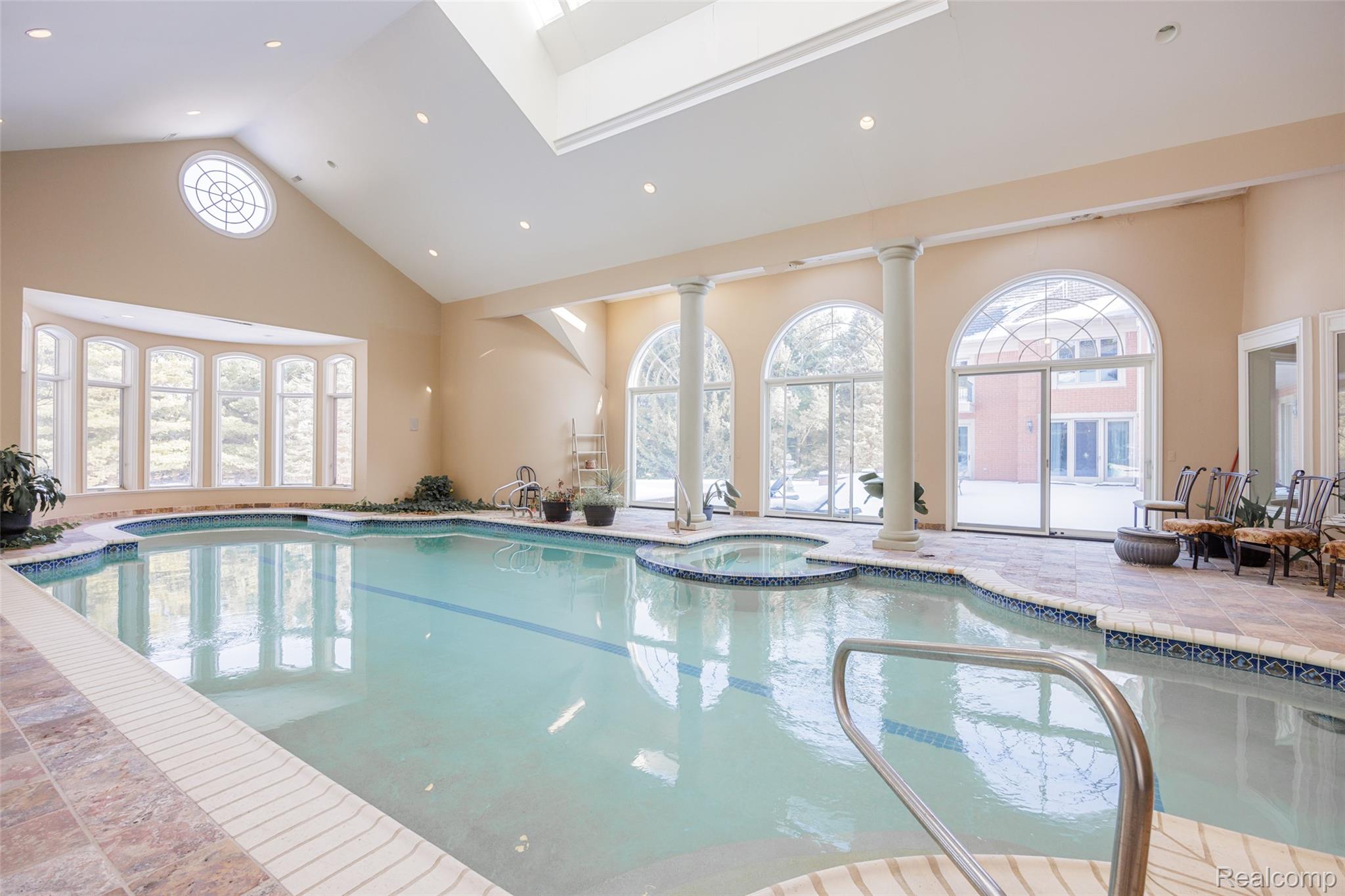 5165 Abbey Drive Rochester, MI 48306 - Photo 37 of 66 Indoor swimming pool with an integrated spa, featuring a vaulted ceiling and multiple skylights