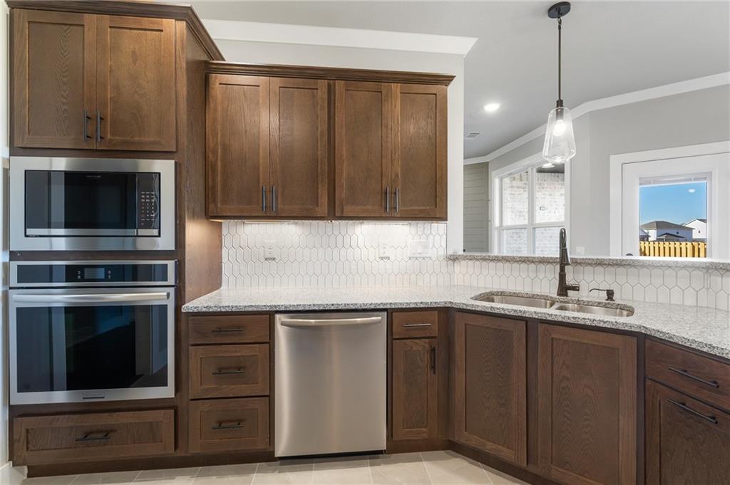 1910 Peacock Road Centerton, AR 72719 - Photo 6 of 29 Kitchen featuring wood-finish cabinetry, stainless steel appliances, speckled countertops, a double basin sink, and a picket tile backsplash