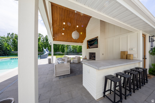 630 East Center Street Alpine, UT 84004 - Photo 84 of 115 Covered outdoor patio featuring a wood-finish ceiling, built-in fireplace, white brick wet bar with seating, and a large swimming pool