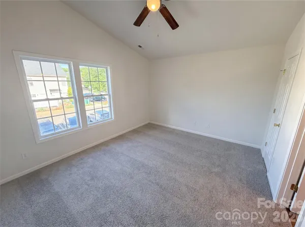 an empty room with chandelier fan and windows