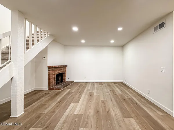a view of an empty room with wooden floor staircase and a kitchen