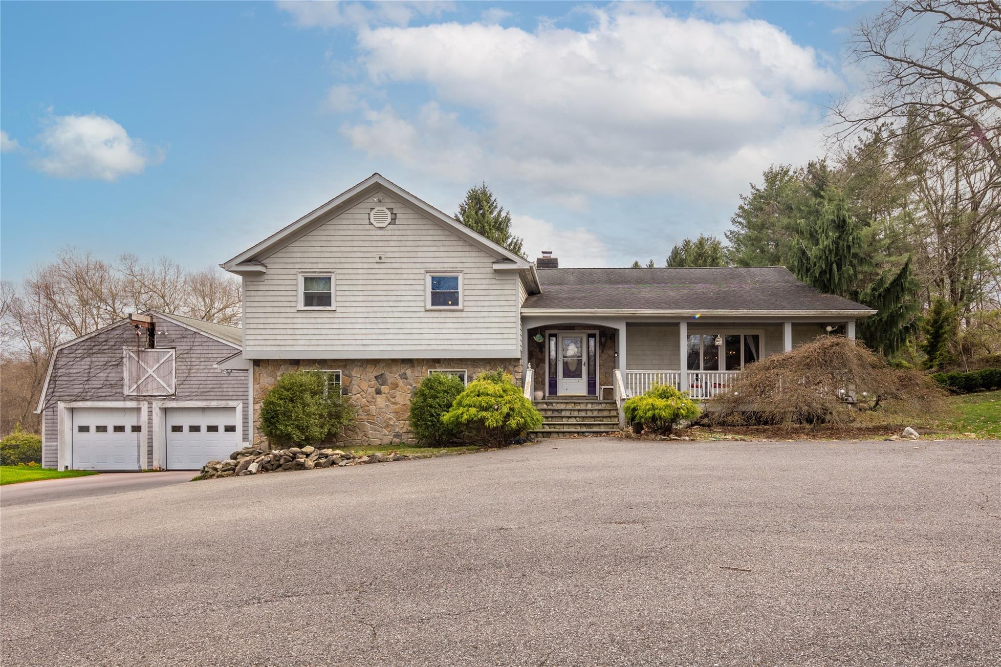 14 Hilltop Road Katonah, NY 10536 - Photo 1 of 1 Split level home featuring a chimney, stone siding, covered porch, an outbuilding, and a garage