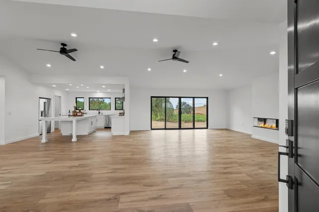 a view of an empty room with wooden floor and a kitchen
